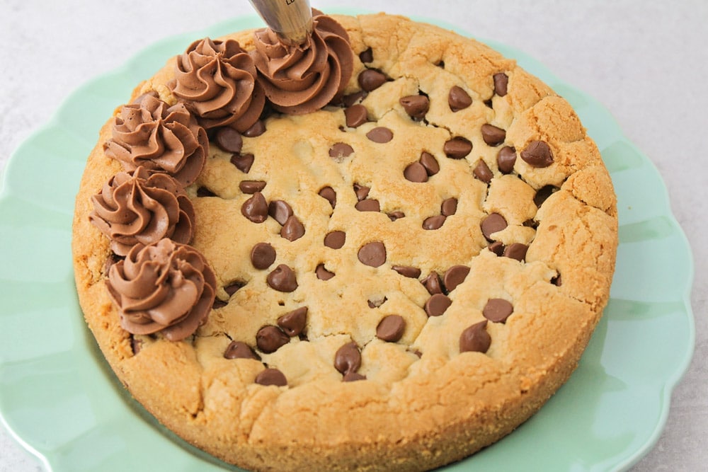 Piping chocolate frosting on chocolate chip cookie cake