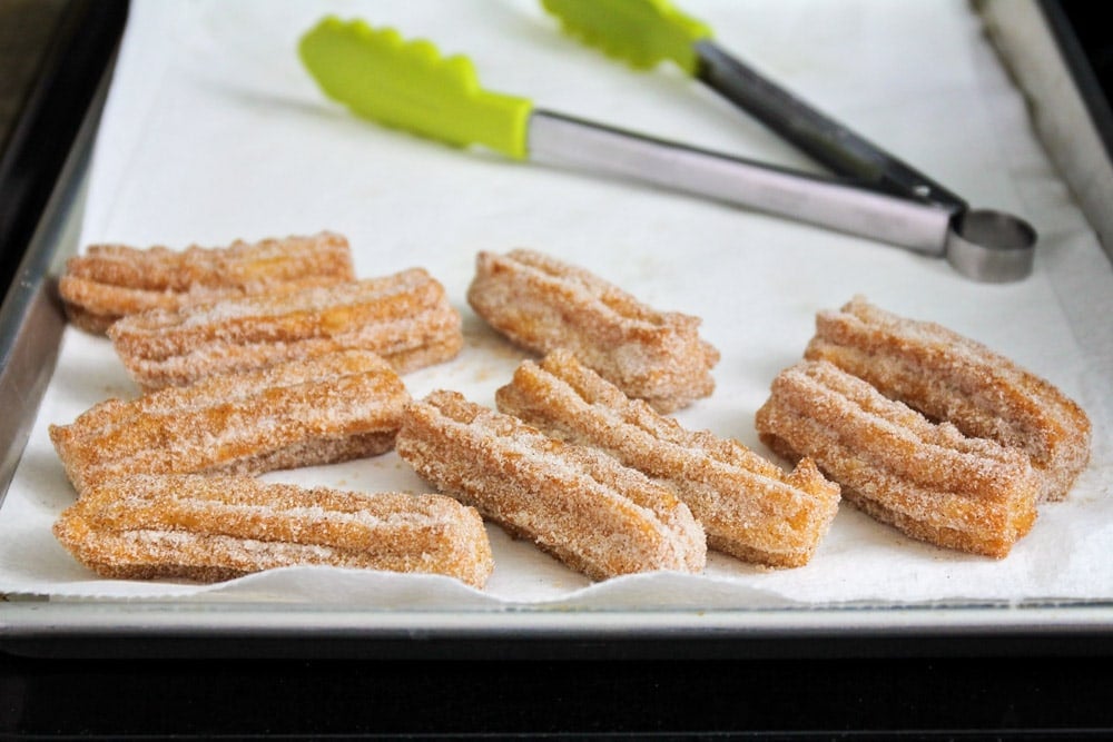 Churros recipe covered in cinnamon and sugar on a baking sheet.