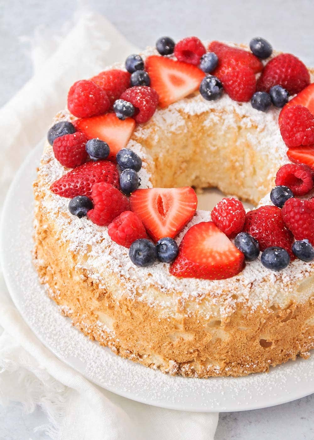 Homemade Angel food cake recipe topped with powder sugar and fresh berries.