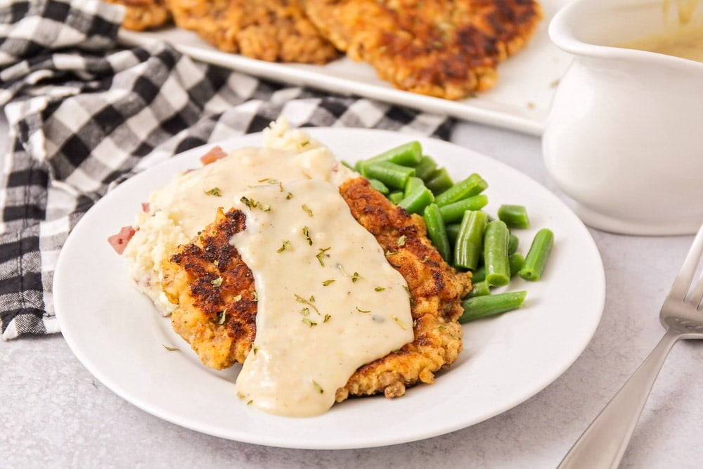 Chicken fried steak served on a white plate with gravy and green beans.