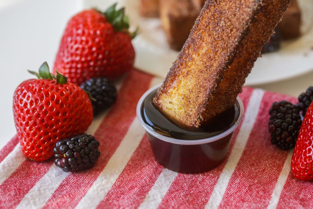 Cinnamon french toast sticks being dipped in syrup.