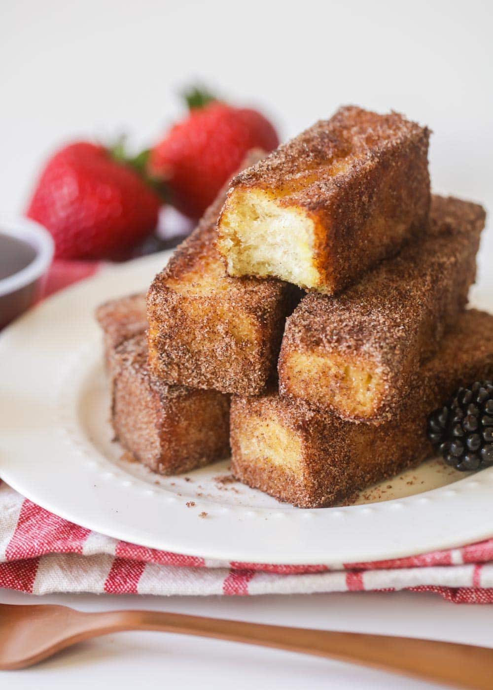 A stack of homemade french toast sticks on a white plate with fresh berries.