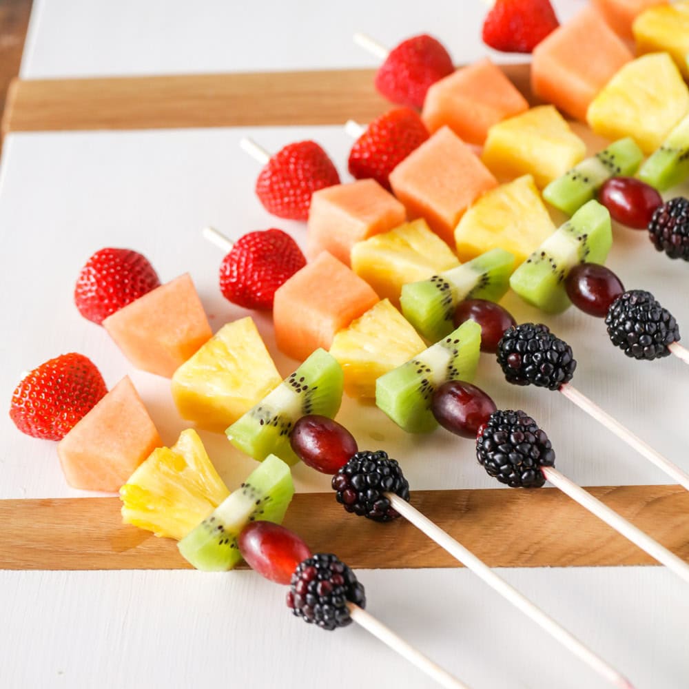 Fruit kabobs on skewers on charcuterie board.