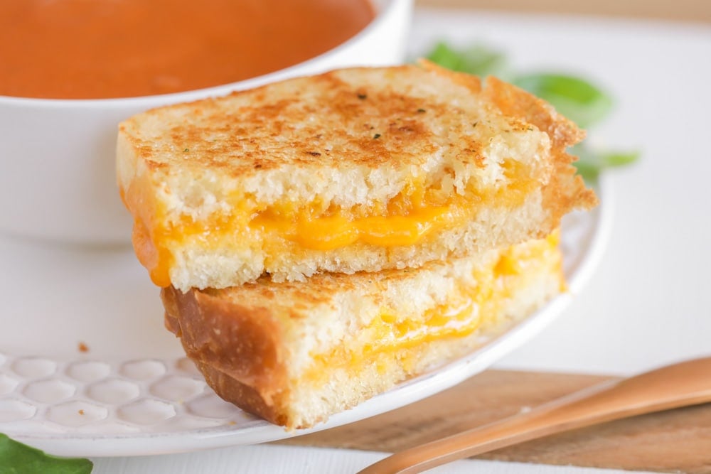 A grilled cheese sandwich cut in half and stacked next to a bowl of soup.