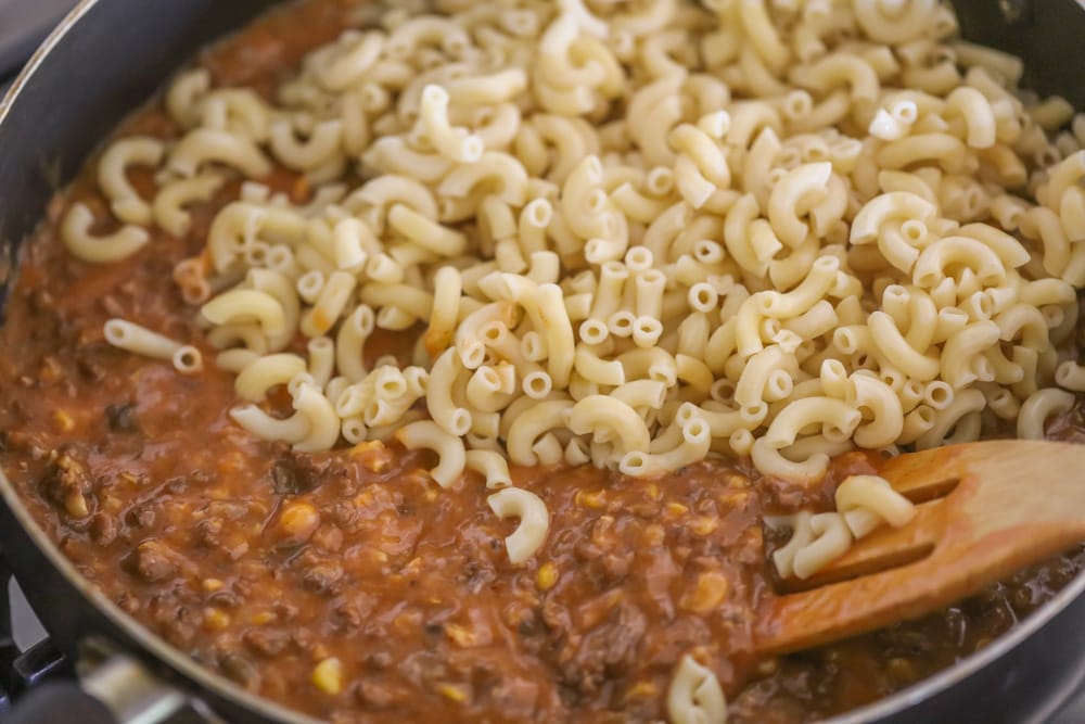 Adding macaroni noodles to a meat mixture in a skillet.