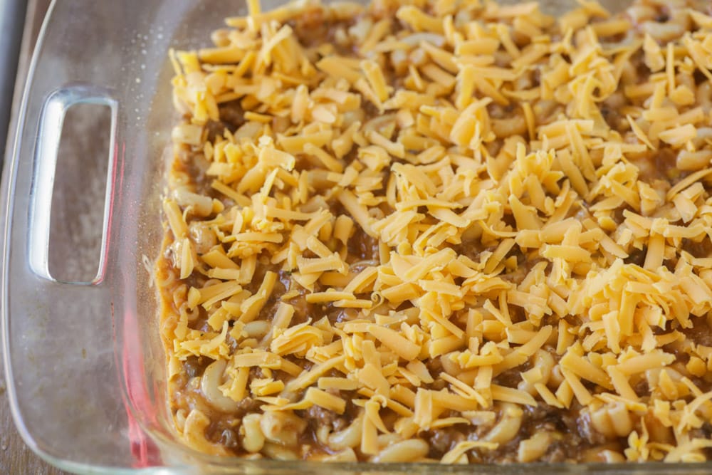 Topping the noodle mixture with shredded cheese.