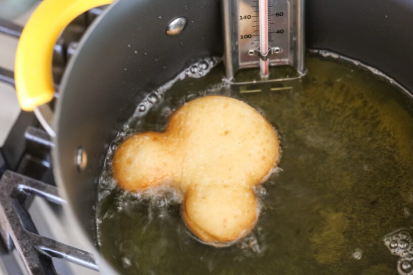Frying a mickey shaped beignet in oil.