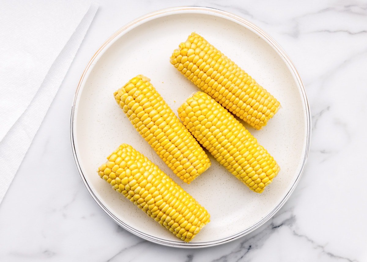Four corn cobs on a white plate.