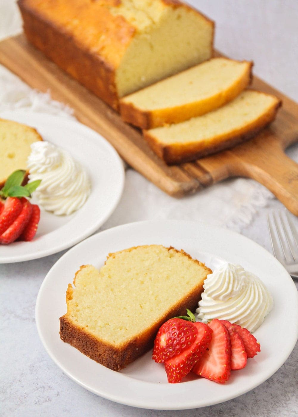 A slice of easy pound cake recipe served with fresh whipped cream and sliced strawberry.