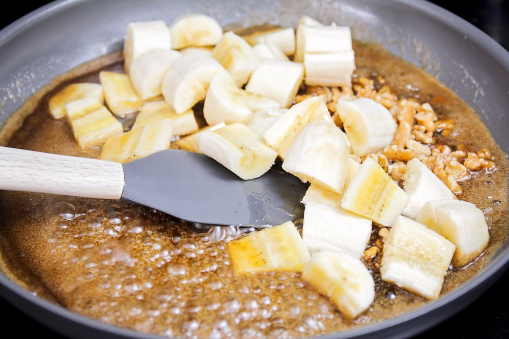 Adding chopped bananas to the sauce in a pan.