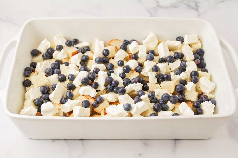 Bread cubes, cream cheese, ad blueberries layered in a casserole dish.