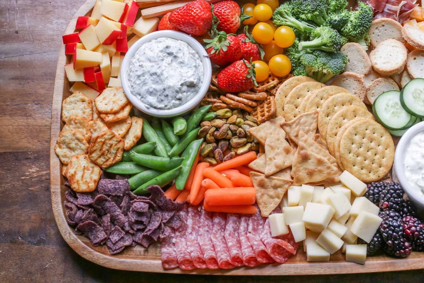 A wooden board piled high with charcuterie ingredients.