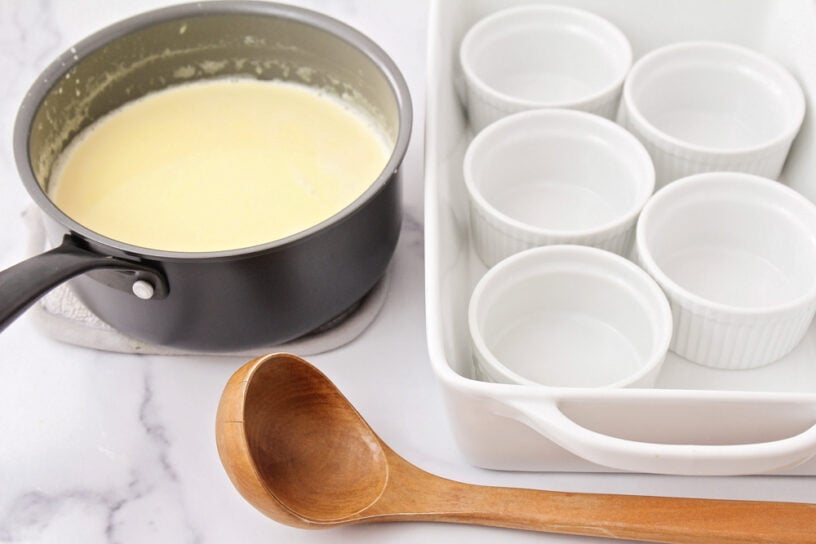 A fancy restaurant-quality crème brûlée is easy to achieve at home!! Just 5 ingredients to create a sugar-crusted creamy vanilla custard! A saucepan of cream next to a baking dish with empty ramekins in it.
