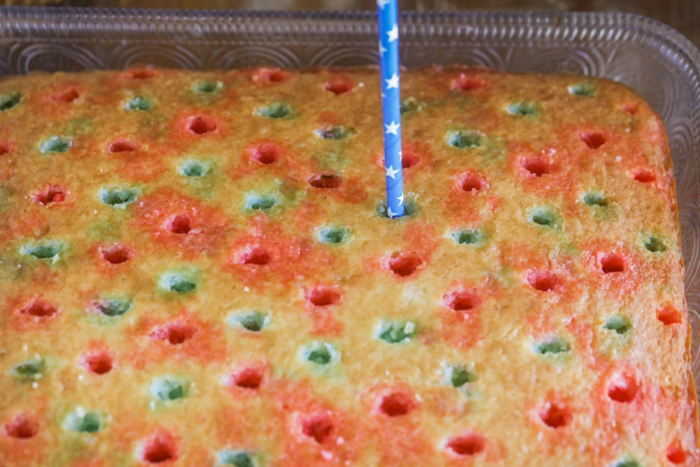 Adding red and blue jello to 4th of July poke cake using a straw. 