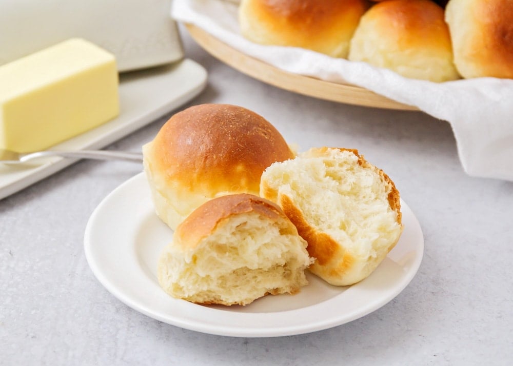 Potato dinner rolls on a plate with one torn in half.