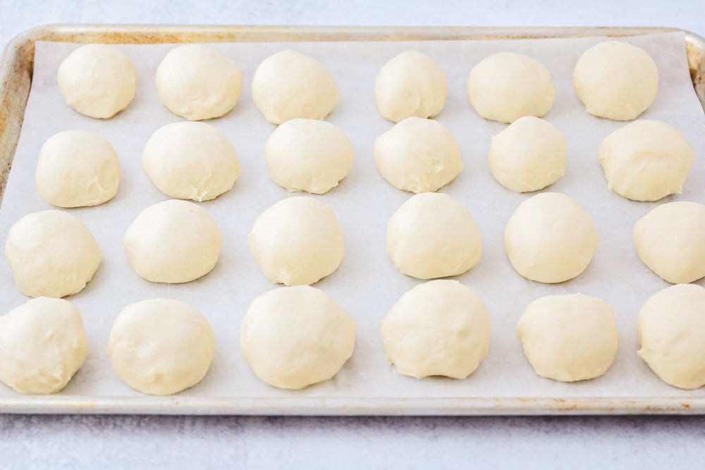 Uncooked dinner rolls on top of parchment paper on a metal pan ready to be baked. 