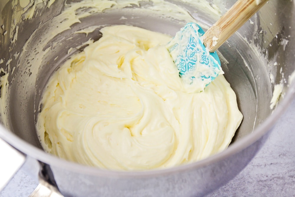 Mixing orange cream cheese frosting in a metal bowl.