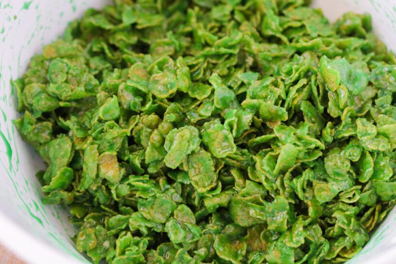 Cornflakes coated in green marshmallow mixture in a mixing bowl for Christmas wreath cookies.