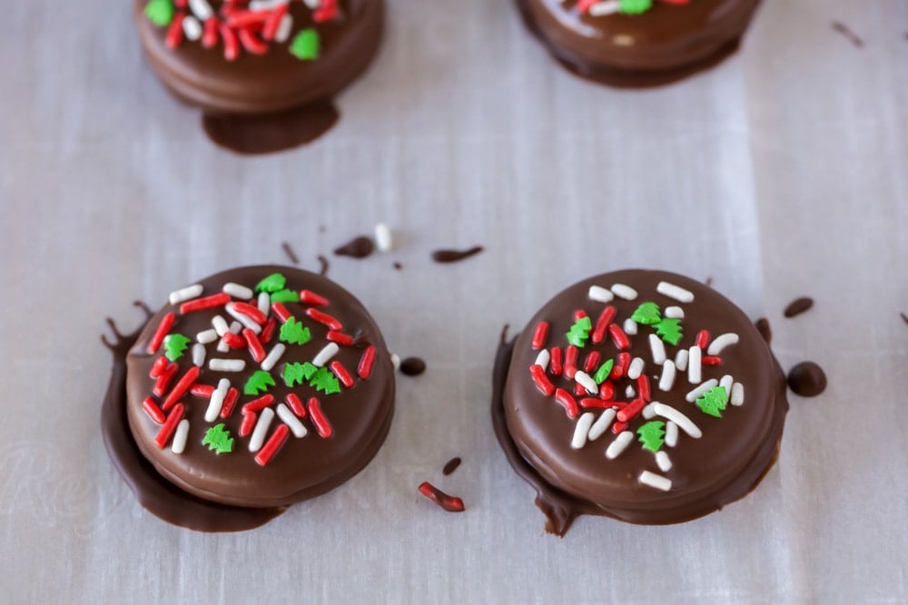 Chocolate covered Oreos with Christmas sprinkles on parchment paper.