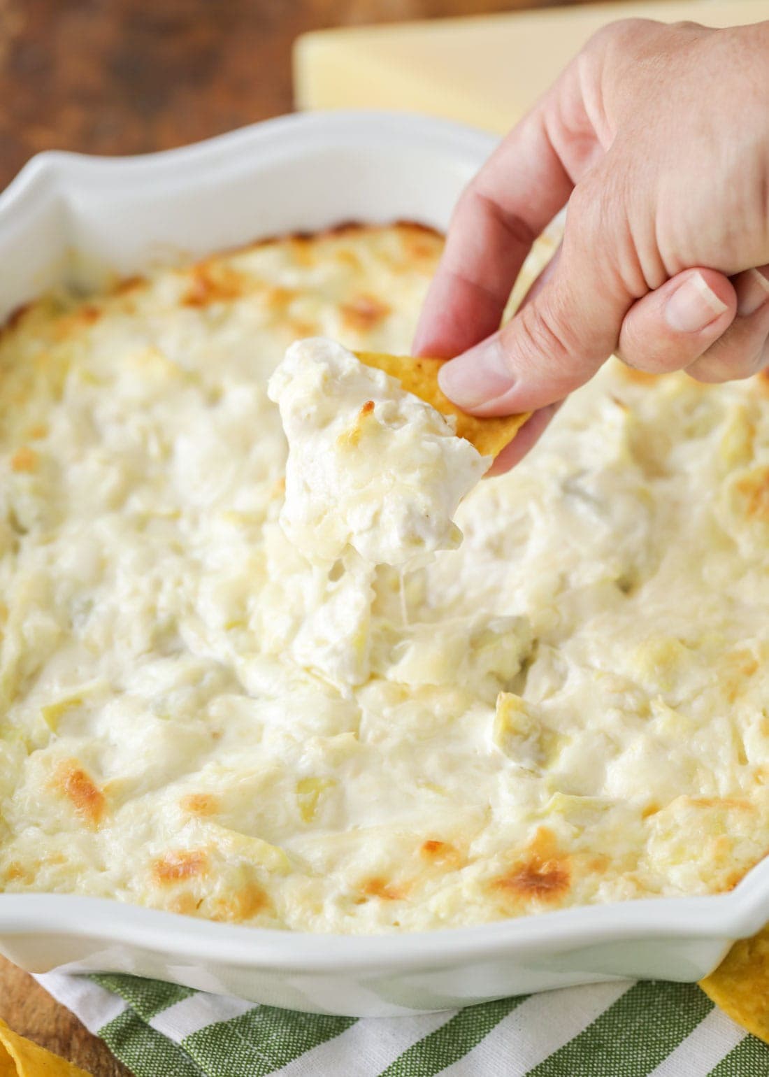 A hand dipping a chip into hot artichoke dip.