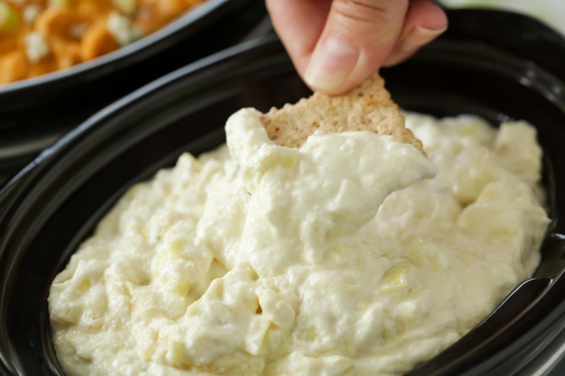 Dipping a cracker into crock pot artichoke dip