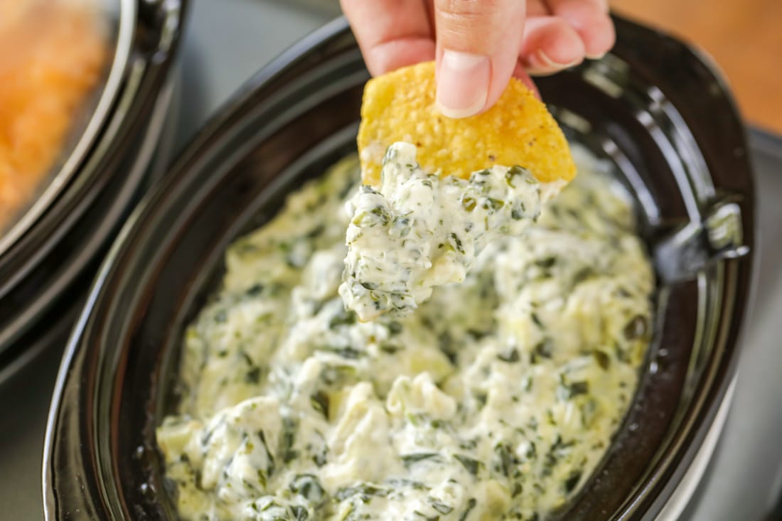 Easy Appetizers - Slow Cooker Artichoke Dip with a chip dipped in the dip in a black crock. 