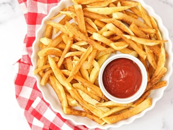 Homemade French fries in a dish with ketchup on the side.