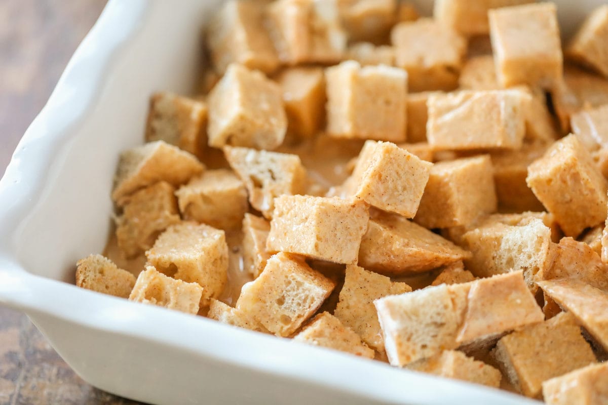 Cubed bread in egg mixture in a white baking pan