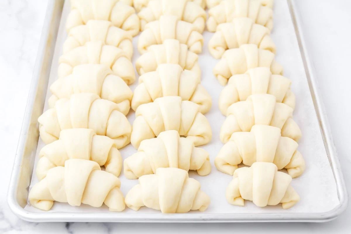 Homemade crescent rolls risen on baking sheet.