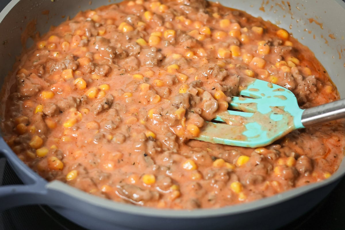 Hamburger casserole ingredients mixed together in skillet.