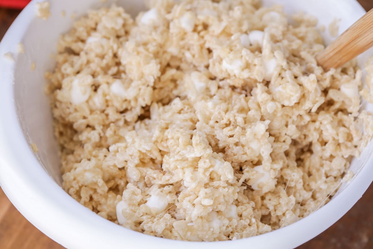 Mixing melted marshmallows and rice krispies in a white bowl.