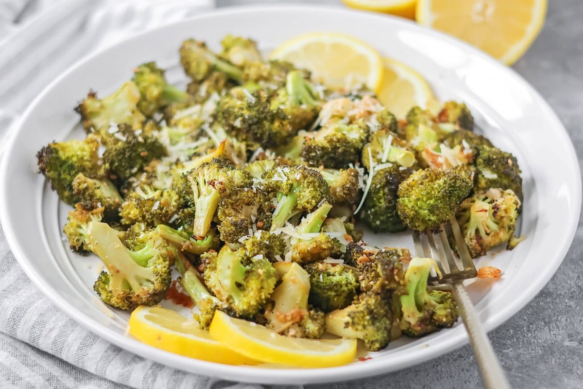 Roasted broccoli recipe on white plate with lemon wedges.