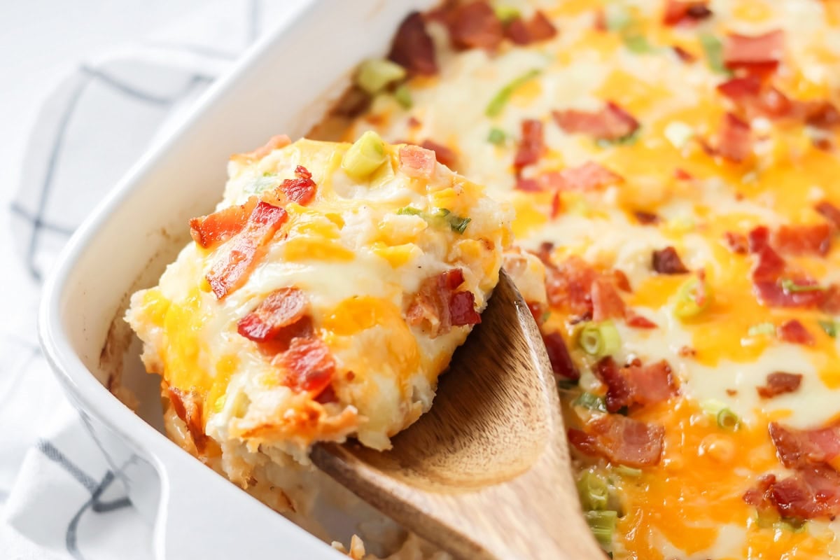 Scooping twice baked potato casserole from a baking dish.