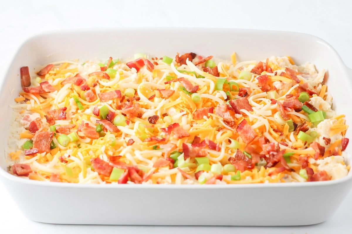 Adding cheese and bacon to the top of a twice baked potato casserole.