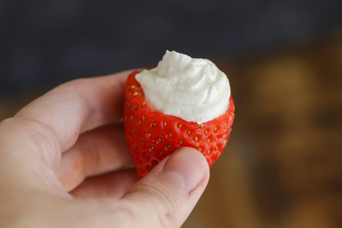 A hand holding one cheesecake stuffed strawberry.