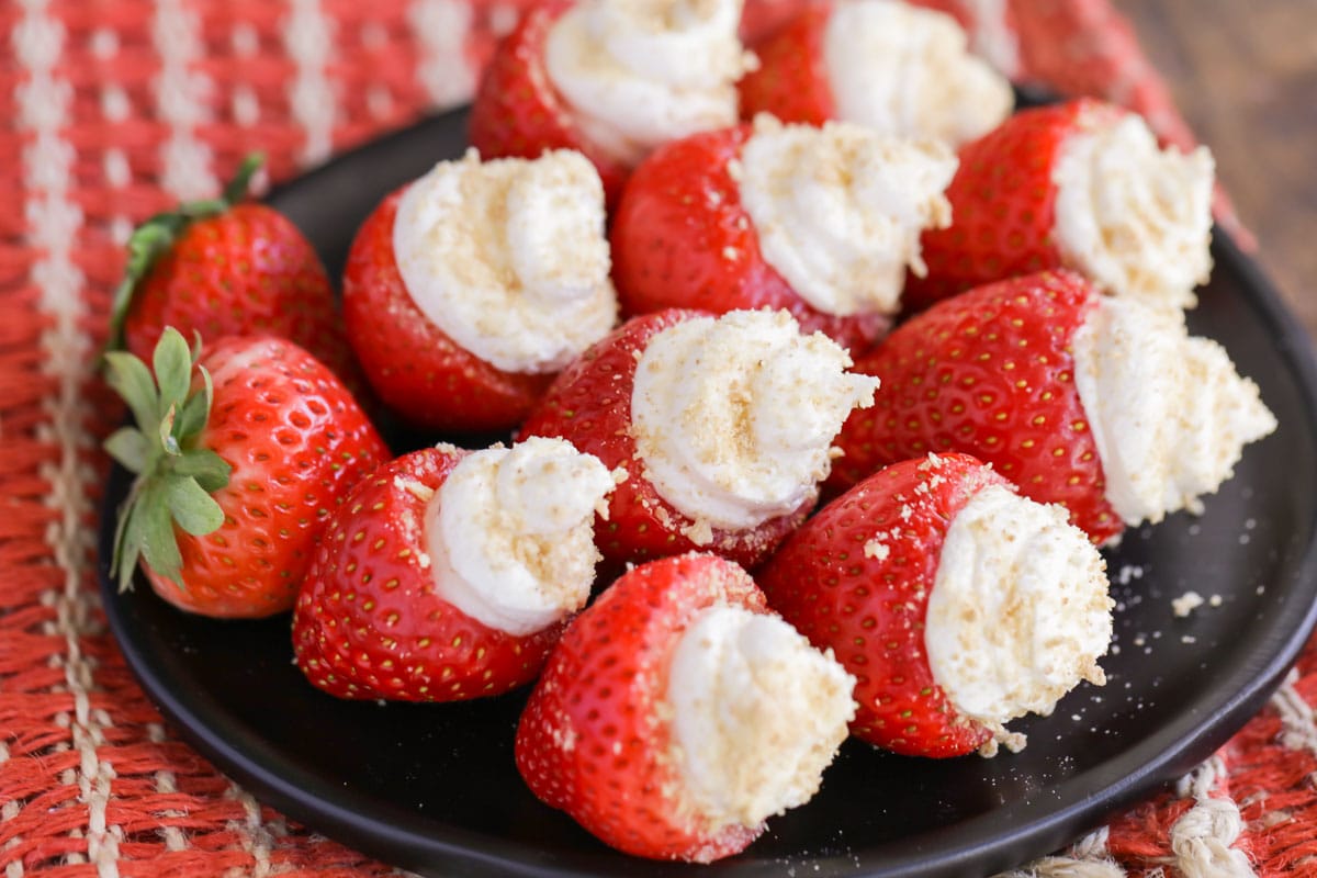 Cheesecake stuffed strawberries served on a black plate.