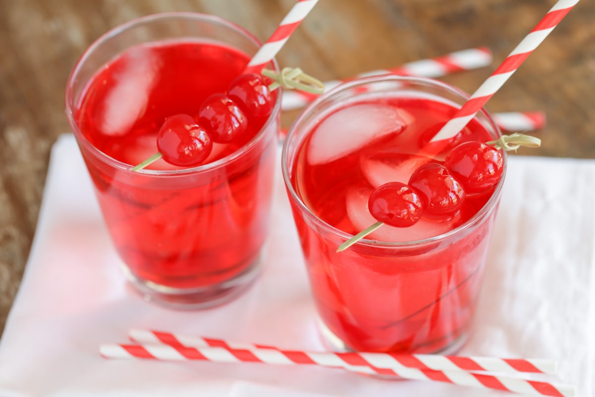 Valentines Dinner Ideas - two Shirley Temple drinks in clear glasses garnished with cherries on cocktail toothpicks and red and white straws. 
