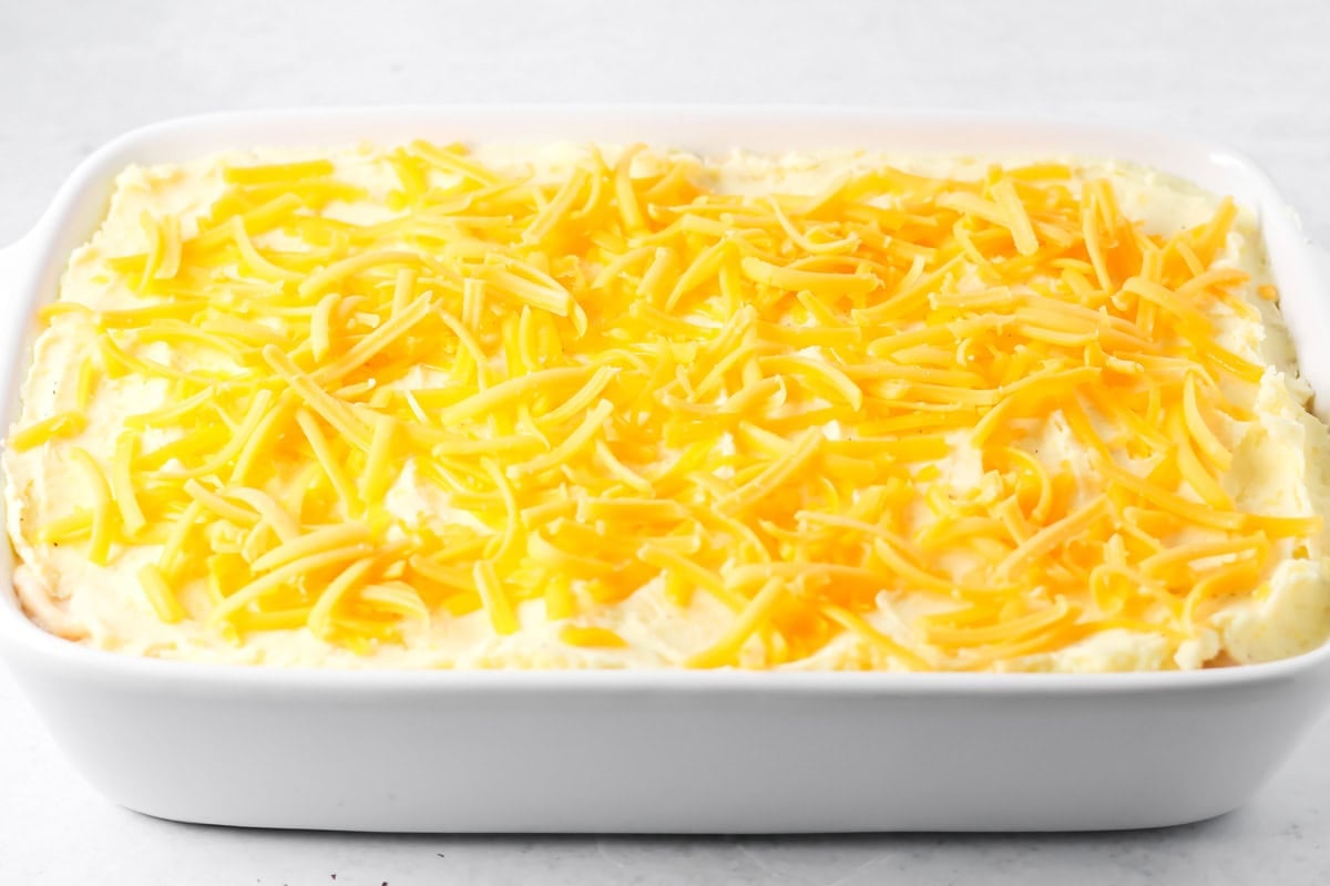 Adding cheese to the top of a thanksgiving leftover casserole.