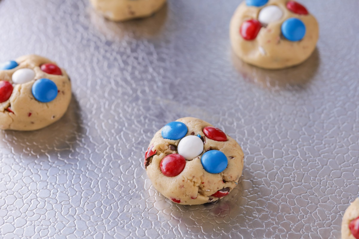 Fourth of July cookie balls filled with M&Ms and lined up on a cookie sheet.