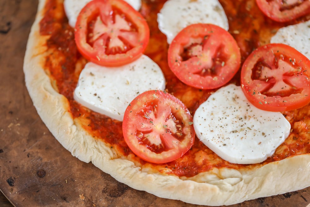 Slices of roma tomatoes and fresh mozzarella on a blind baked pizza crust.
