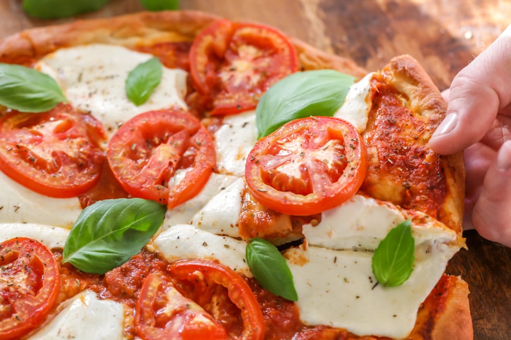 Hand grabbing a slice of margherita pizza.