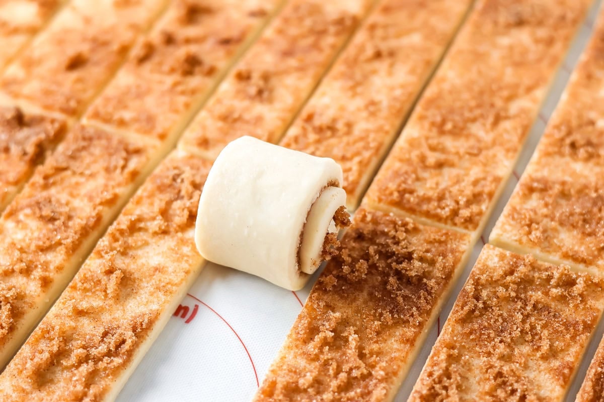 Rolling dough strips to make mini cinnamon rolls.