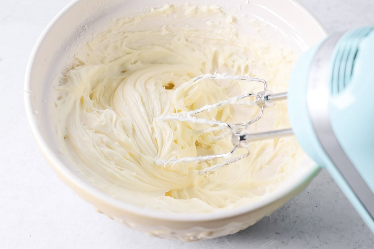 Whipping mini cinnamon rolls frosting in a white bowl.