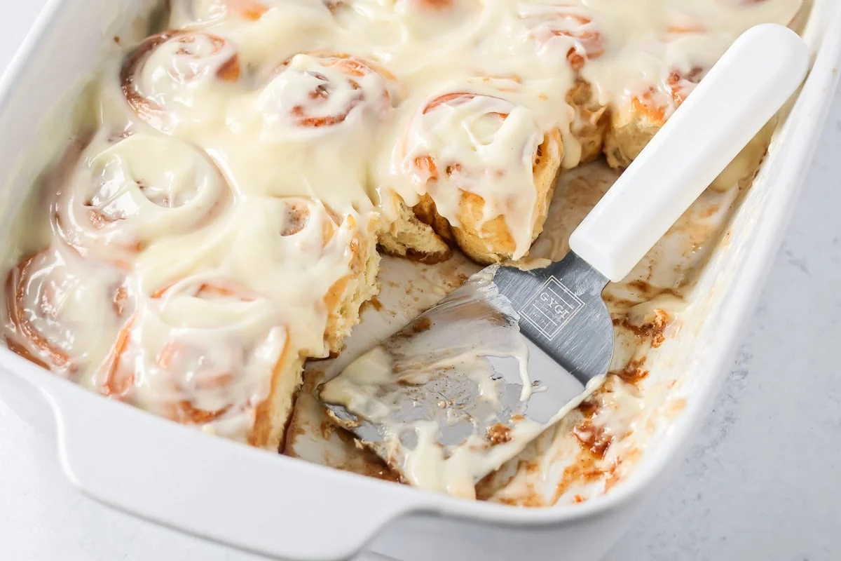 Scooping mini cinnamon rolls recipe from a baking dish.