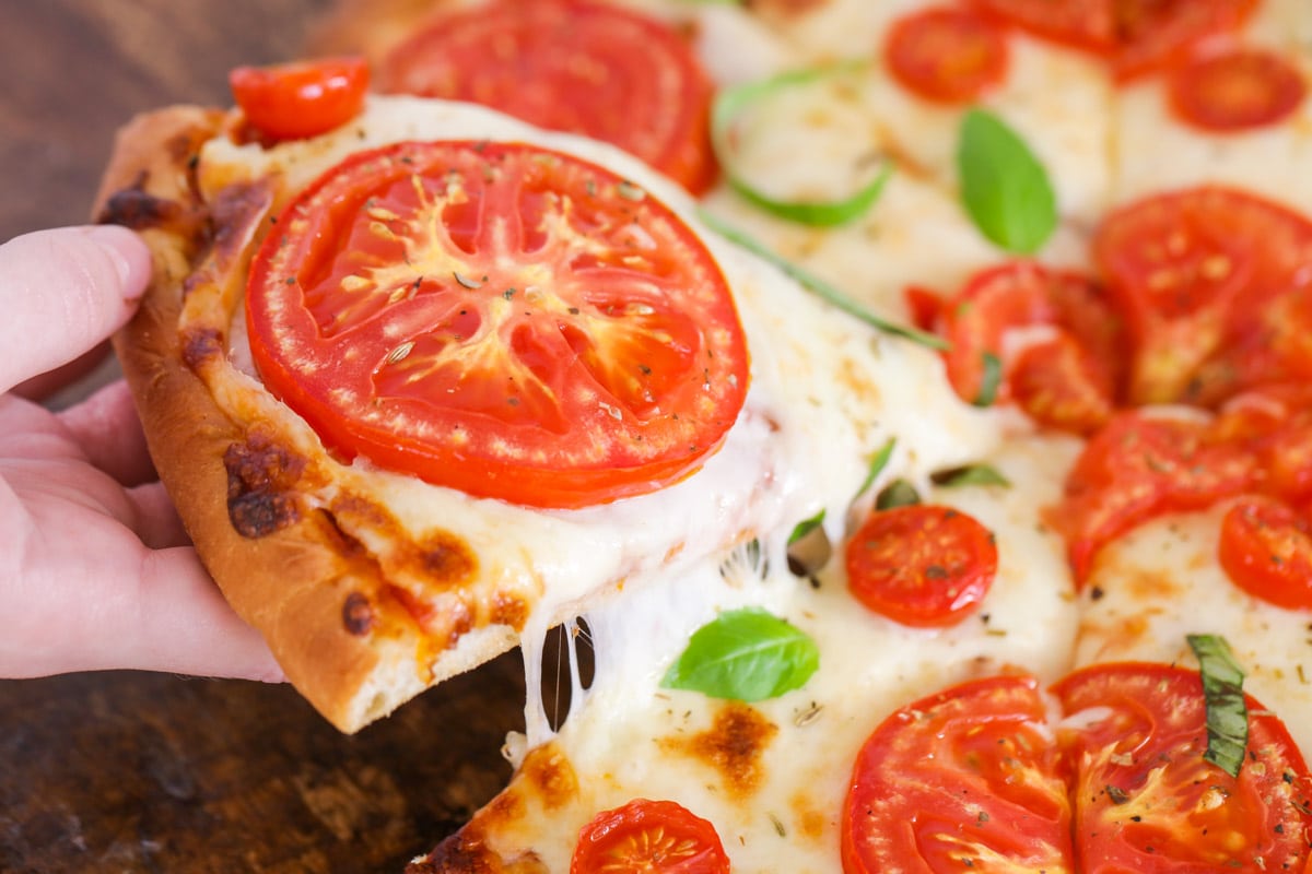 A hand grabbing a slice of tomato pizza