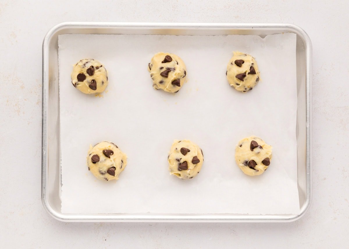 Cookie dough balls on a lined baking sheet ready to bake.