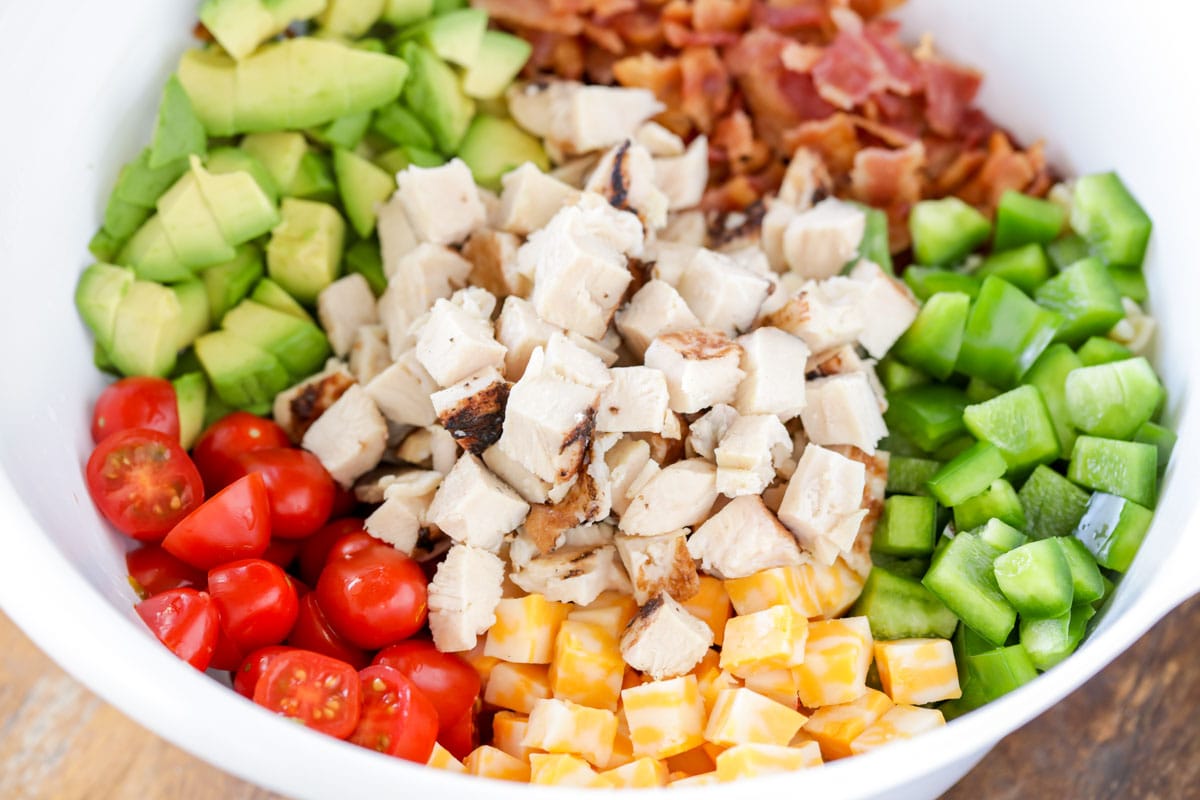 Diced tomato, chicken, avocado, bacon, cheese, and peppers in a white bowl.