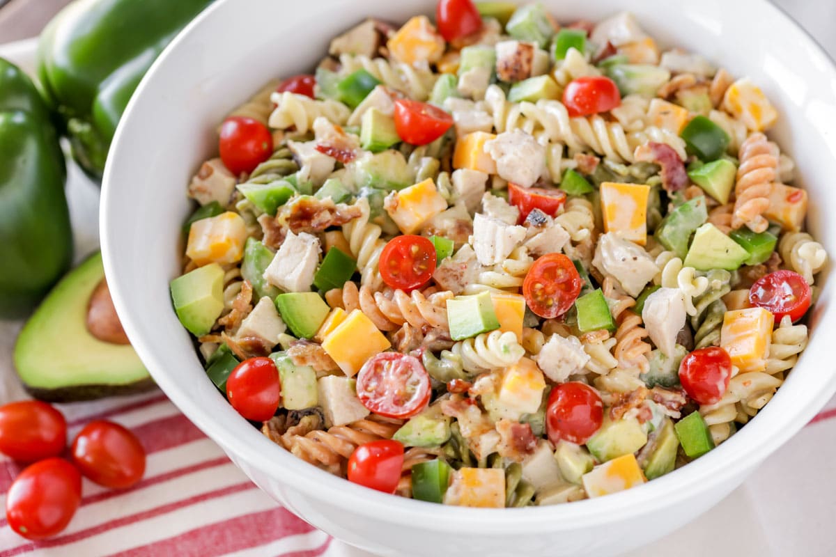 4th of July Recipes - Chicken pasta salad with rotini, tomatoes, cheese, and avocado in a white bowl. 
