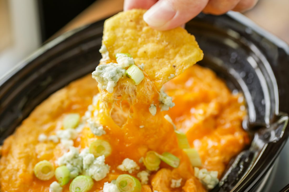 Dipping a tortilla chip in crockpot buffalo chicken dip .