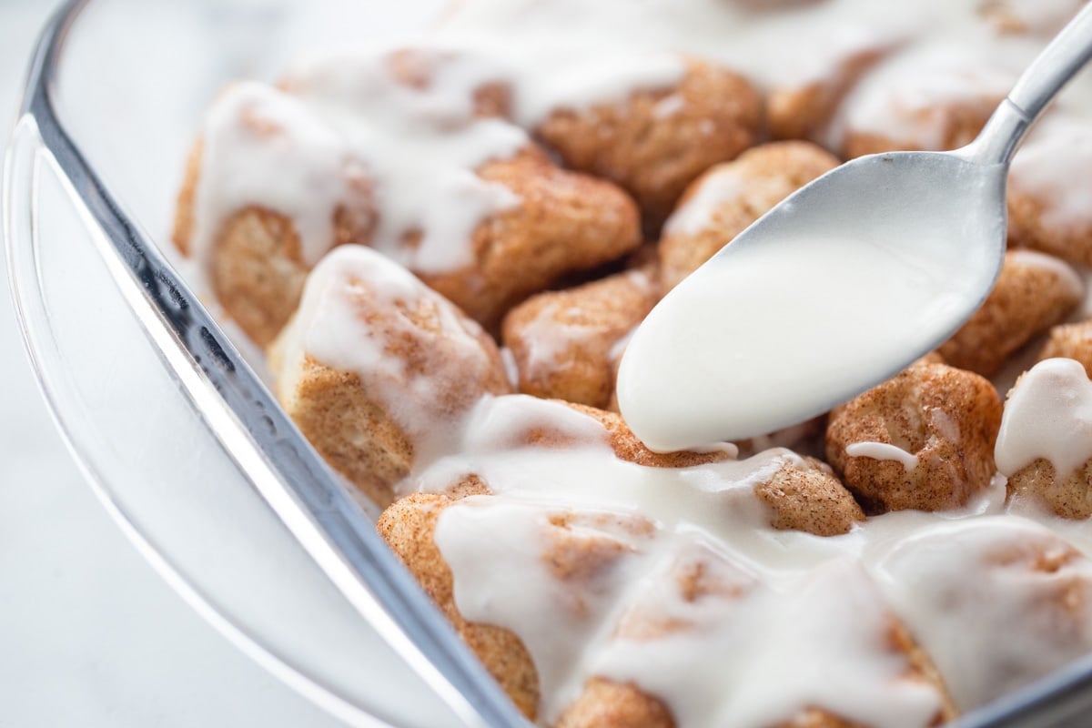 Easy Breakfast Ideas - Cinnamon roll bites with a spoonful of frosting in a glass baking dish. 